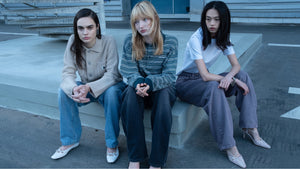 Three women sit on a concrete ledge, with one wearing a striped Carhartt WIP sweater.